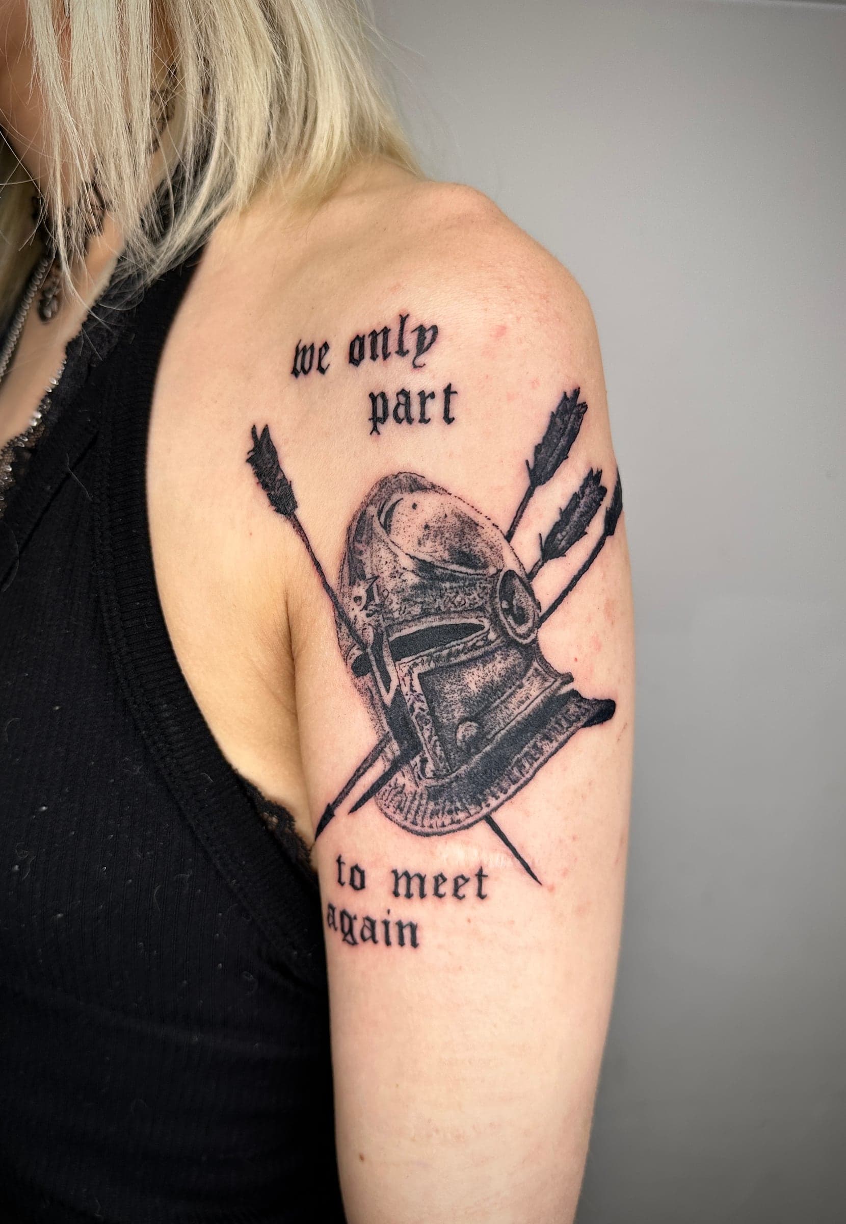 Illustratives Tattoo eines Ritterhelms mit gekreuzten Pfeilen, Oberarm